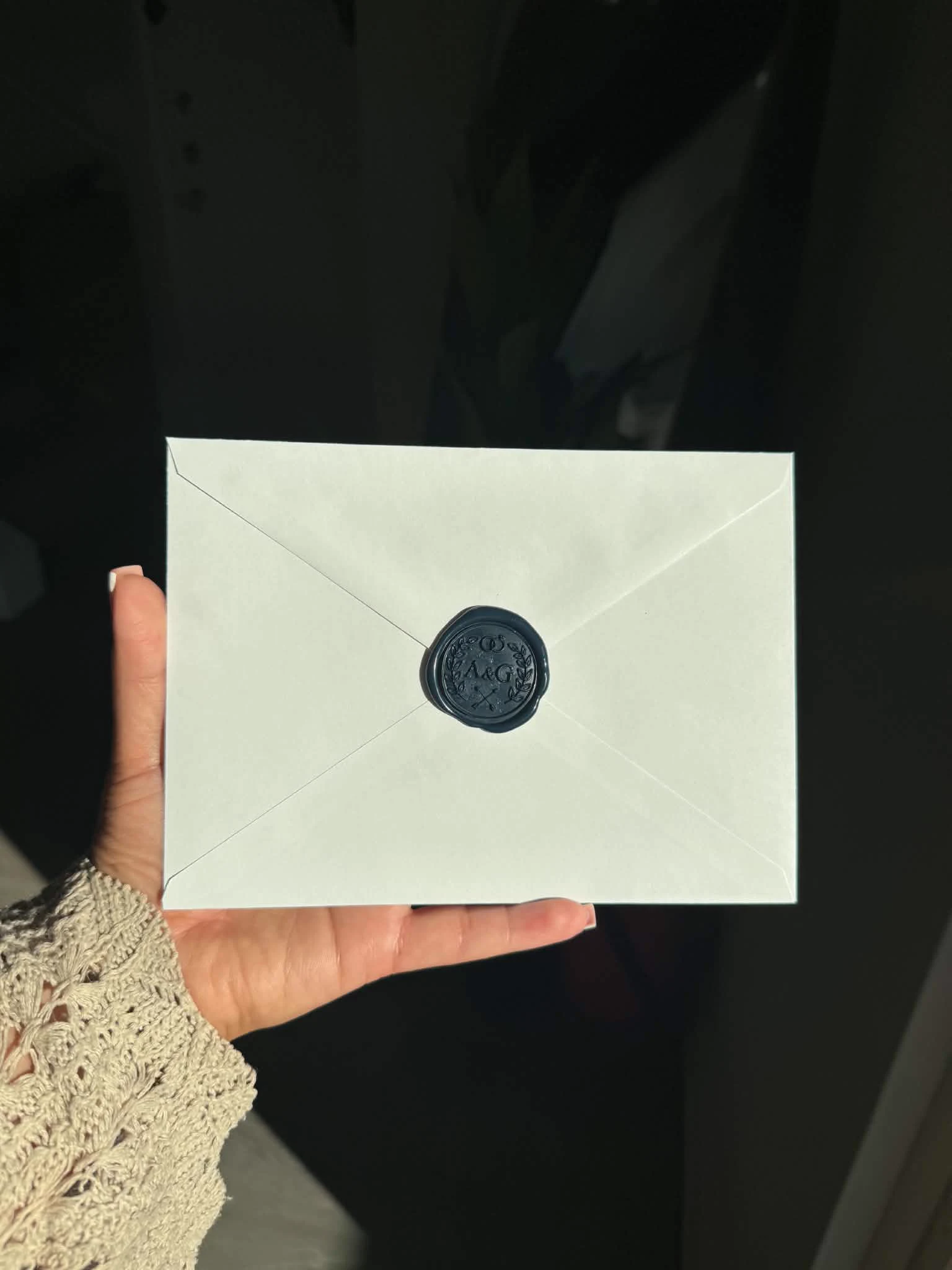 Hand holding a white envelope closed with a custom dark wax seal